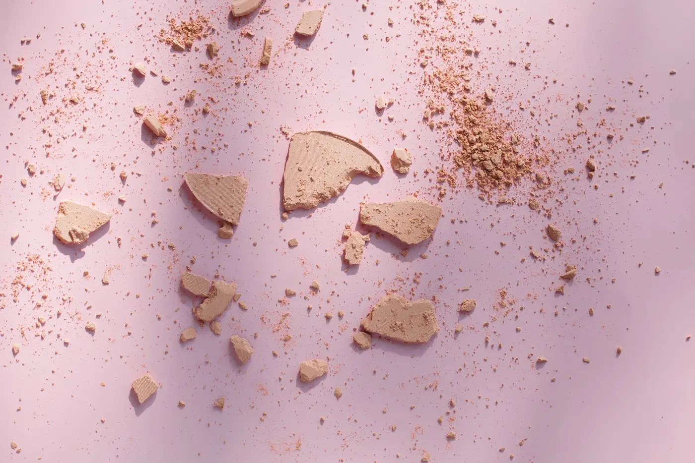 Zerbrochene Puderstücke und -krümel auf rosa Hintergrund