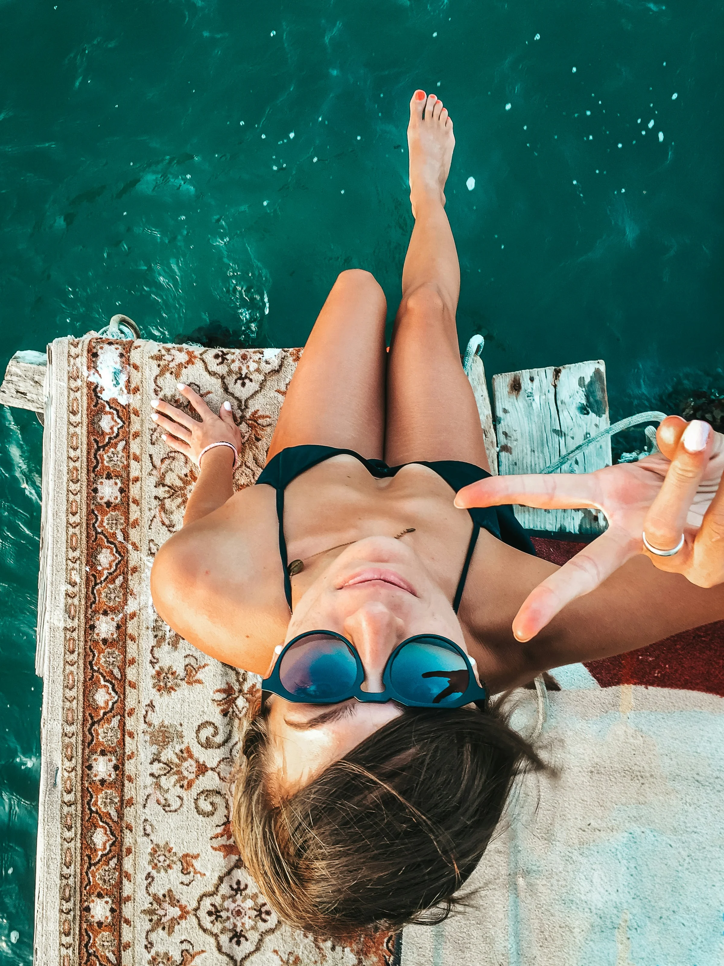Frau mit Sonnenbrille sonnt sich auf einem Holzsteg am türkisblauen Wasser