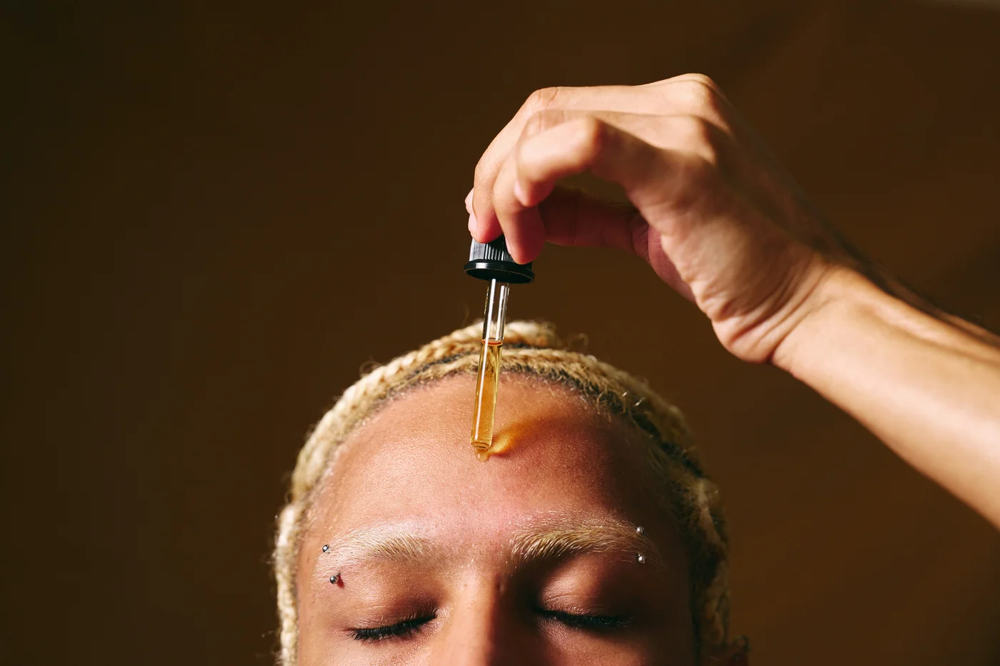 Close-up auf ein Gesicht, angeschnitten. Ein Mann trägt sich mit einer Pipette Öl auf die Stirn