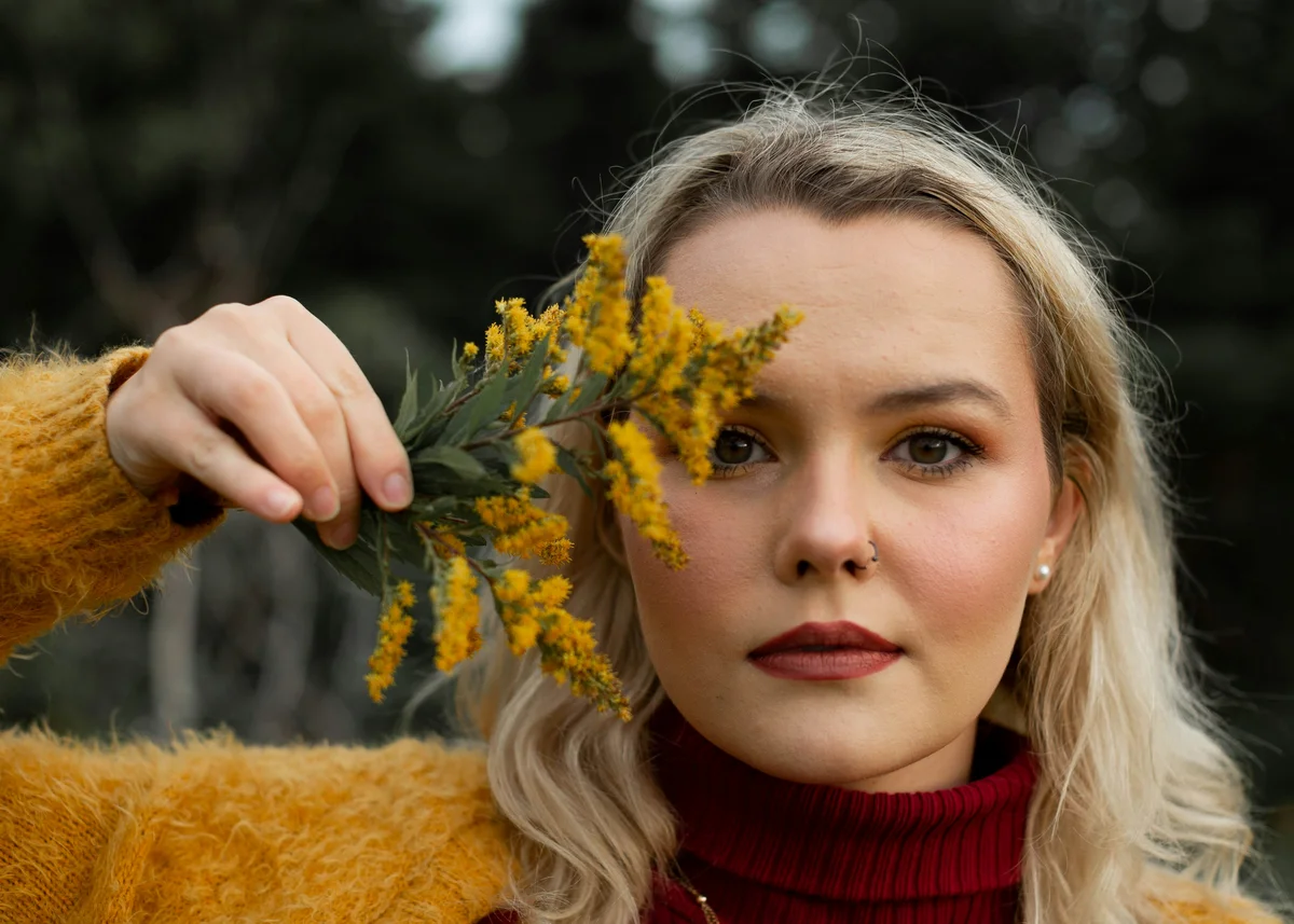 Frau im Pulli mit Pflanze vor dem Gesicht und herbstlichen Makeup