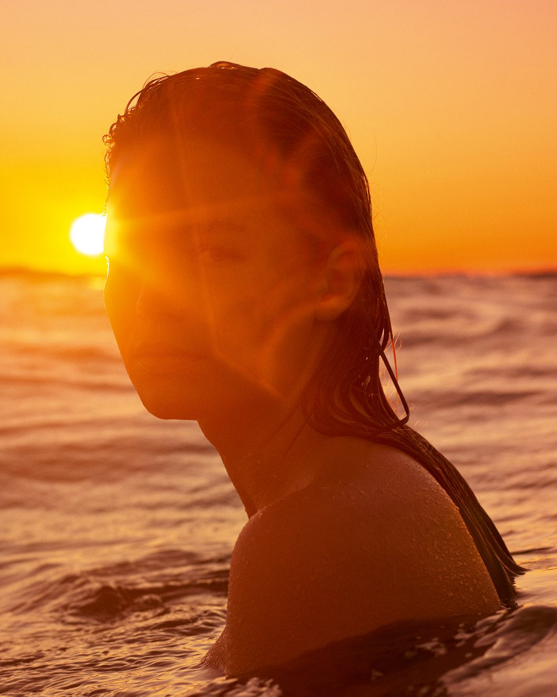 Vor der untergehenden Sonne schwimmt eine Frau im Meer
