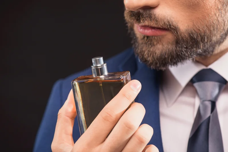 Mann im Anzug riecht an Parfum