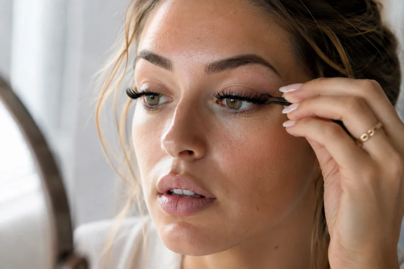 Frau setzt sich mit einer schwarzen Pinzette künstliche Wimpern am oberen Wimpernkranz an