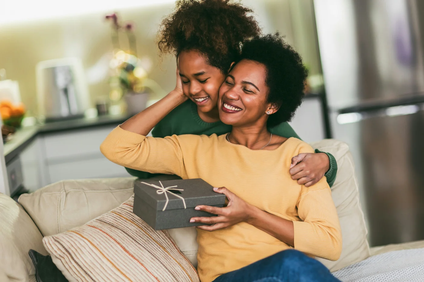 frau-und-madchen-zu-hause-feiern-muttertag-sitzen-auf-dem-sofa-tochter-halt-geschenkbox-fur-mutter-