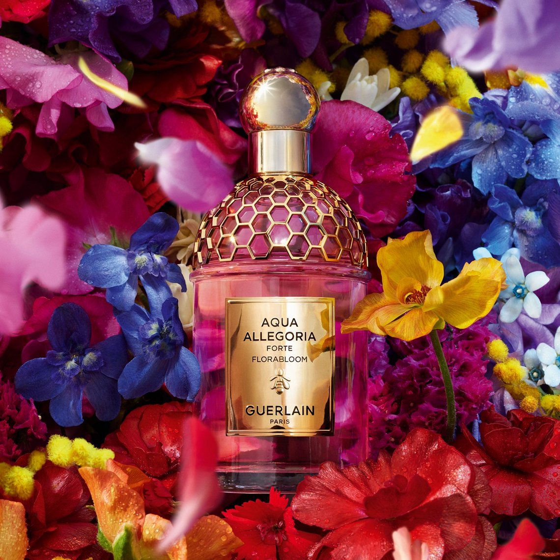 Guerlain Aqua Allegoria Florabloom Forte Eau de Parfum Flakon mit goldenem Etikett inmitten eines üppigen Meeres aus farbenprächtigen Blüten.