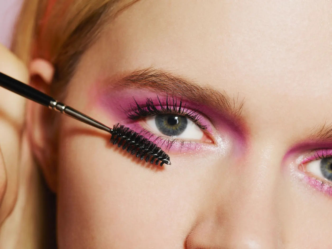 Frau mit rosa Augen-Make-up trägt Mascara auf