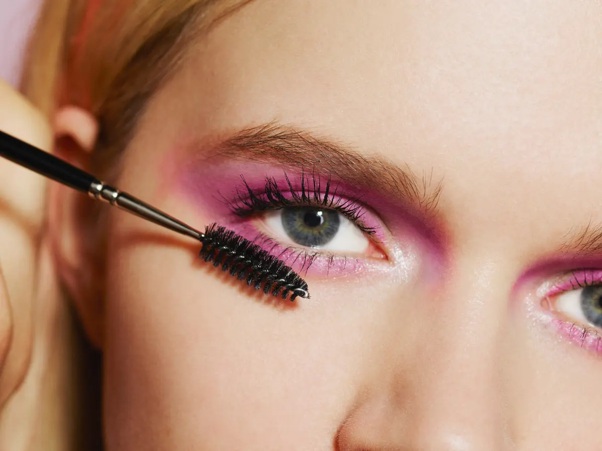 Frau mit rosa Augen-Make-up trägt Mascara auf