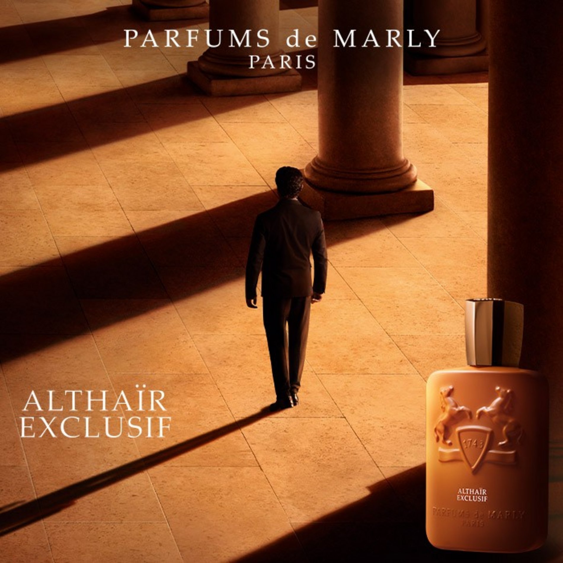 Parfums de Marly Althaïr Exclusif: Flakon in Cognacbraun vor einem Mann im Anzug, der durch eine sonnige Säulenhalle mit langen Schatten geht