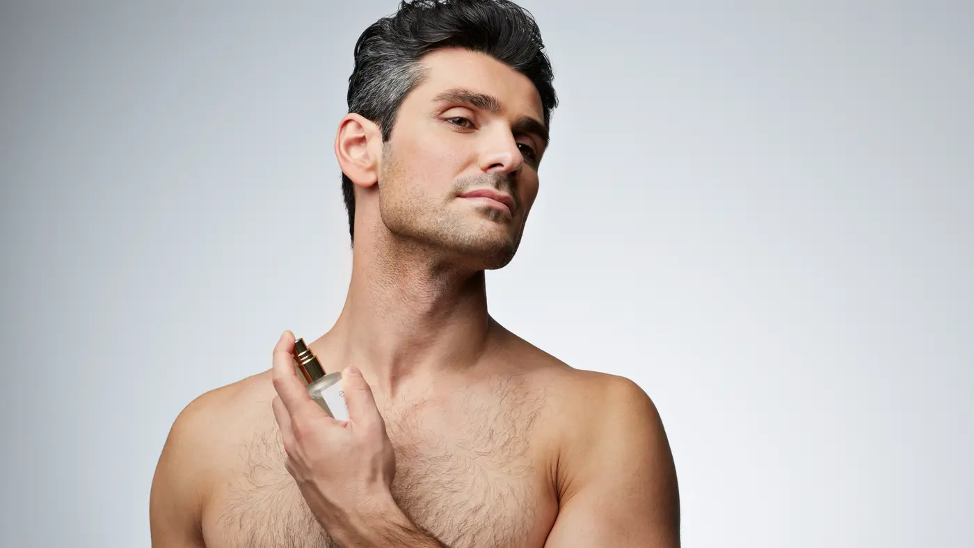 Grau melierter Mann sprüht Parfum auf den Hals