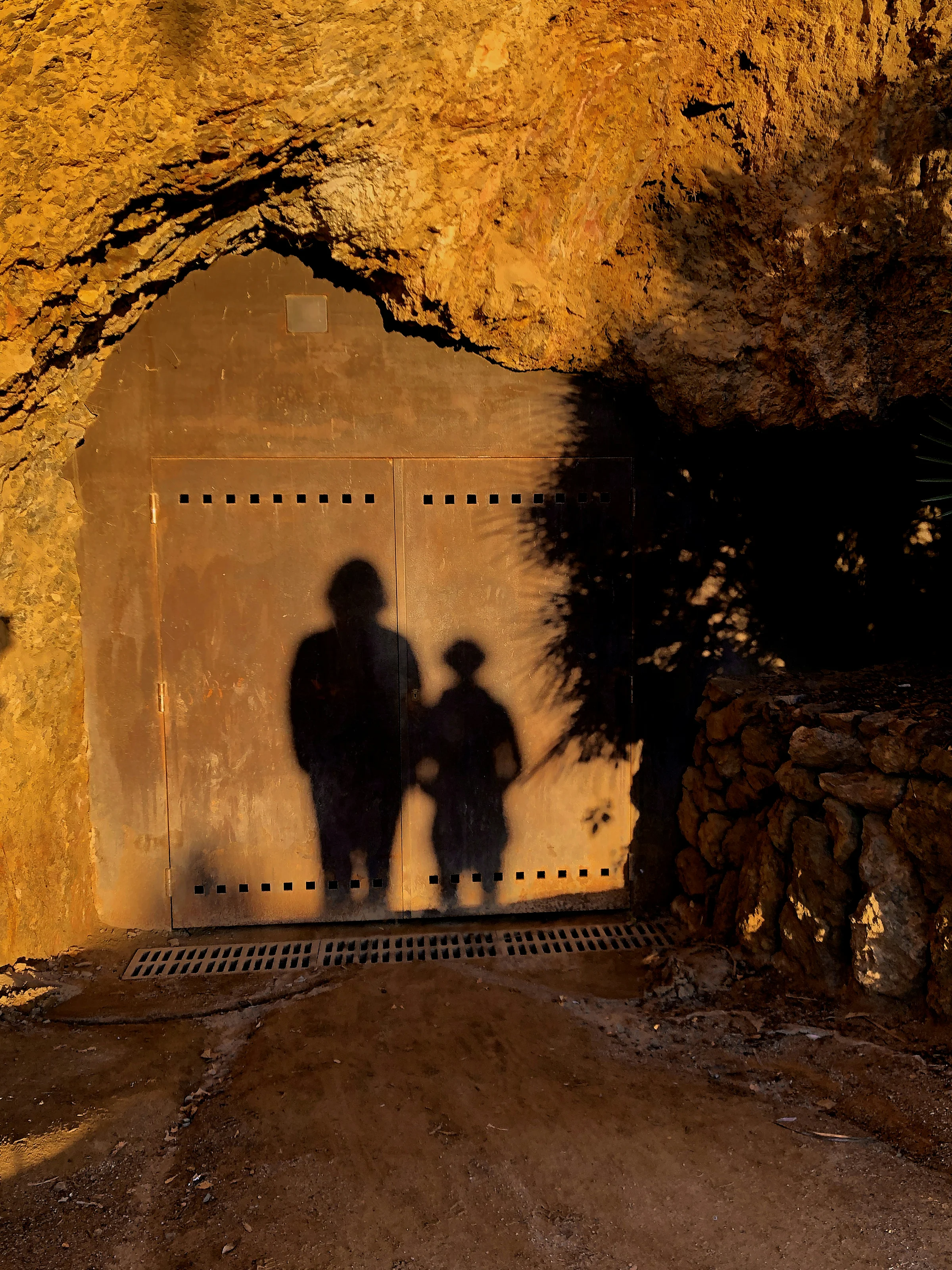 Schatten von zwei Personen auf einer Metalltür in einem Felsdurchgang bei warmem Abendlicht