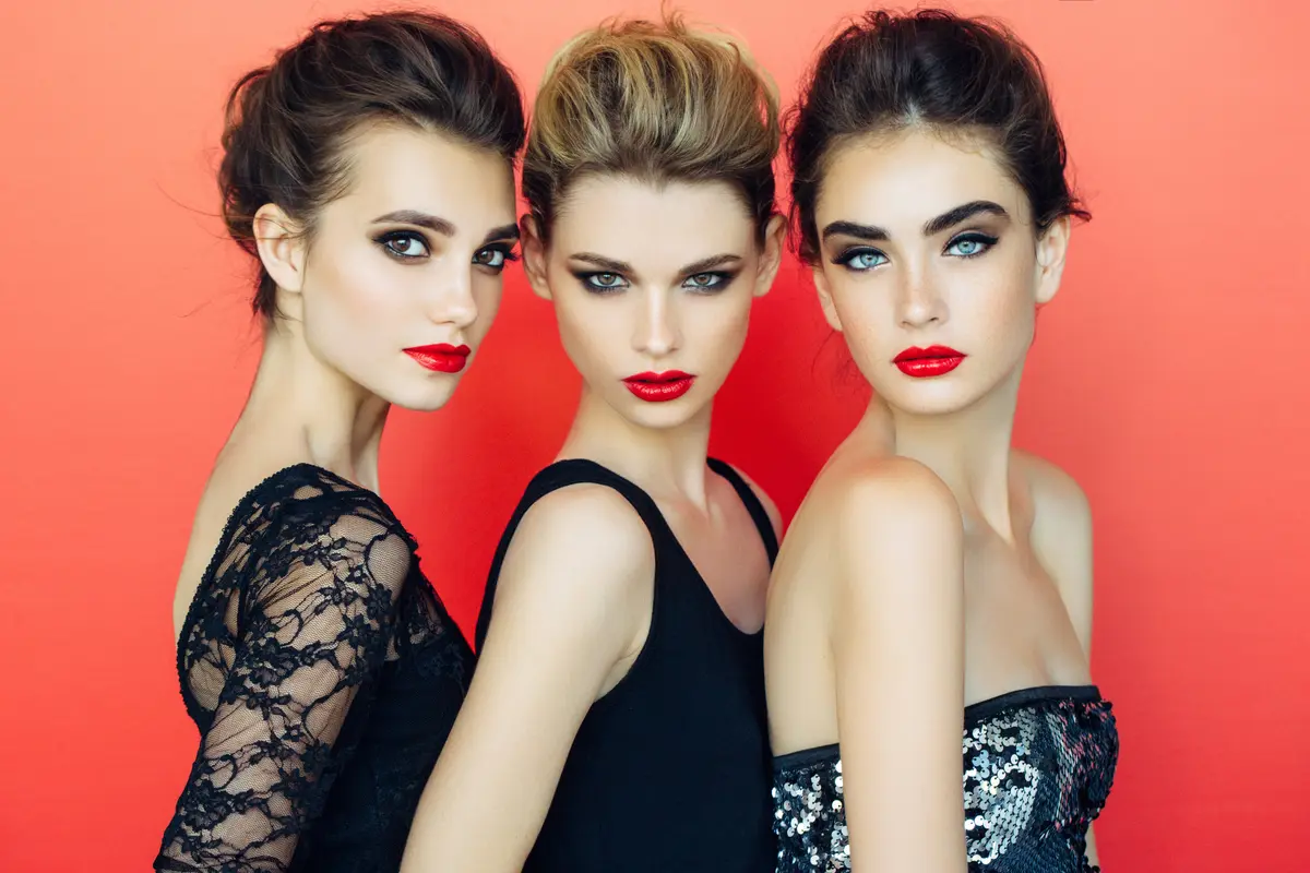 Drei geschminkte Frauen vor rotem Hintergrund