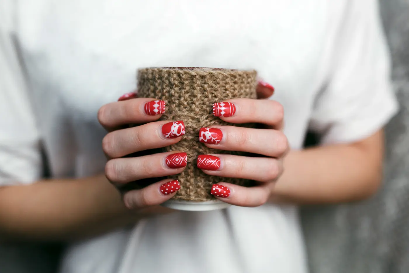 Frau mit weihnachtlichem Nagellack hält Tasse