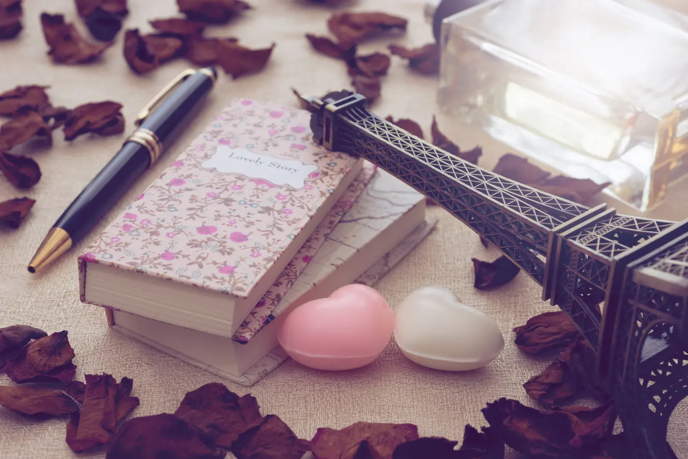 Vintage Miniatur-Eiffelturm mit Rosenblättern, Parfum, Notizbüchern und Herzen