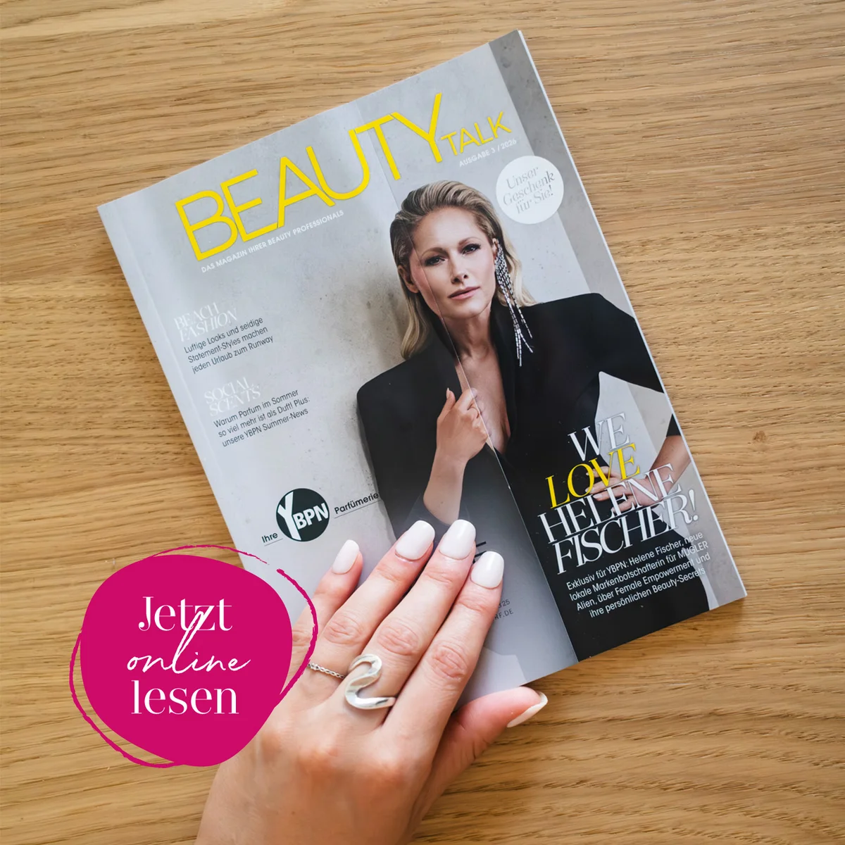 Beauty Talk Magazin Ausgabe 3/2026 auf einem Holztisch, gehalten von einer Hand mit gepflegten Nägeln. Titelthema: „We Love Helene Fischer!" – das YBPN-Kundenmagazin Ihrer Beauty Professionals. Unten links pinker Button mit der Aufschrift „Jetzt online lesen".