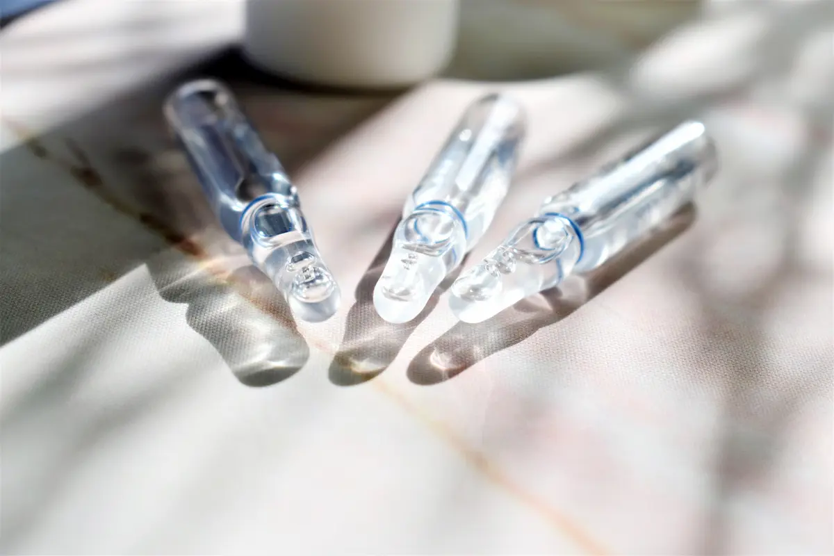 Drei Ampullen mit flüssigem Inhalt liegen auf einem Tisch in der Sonne