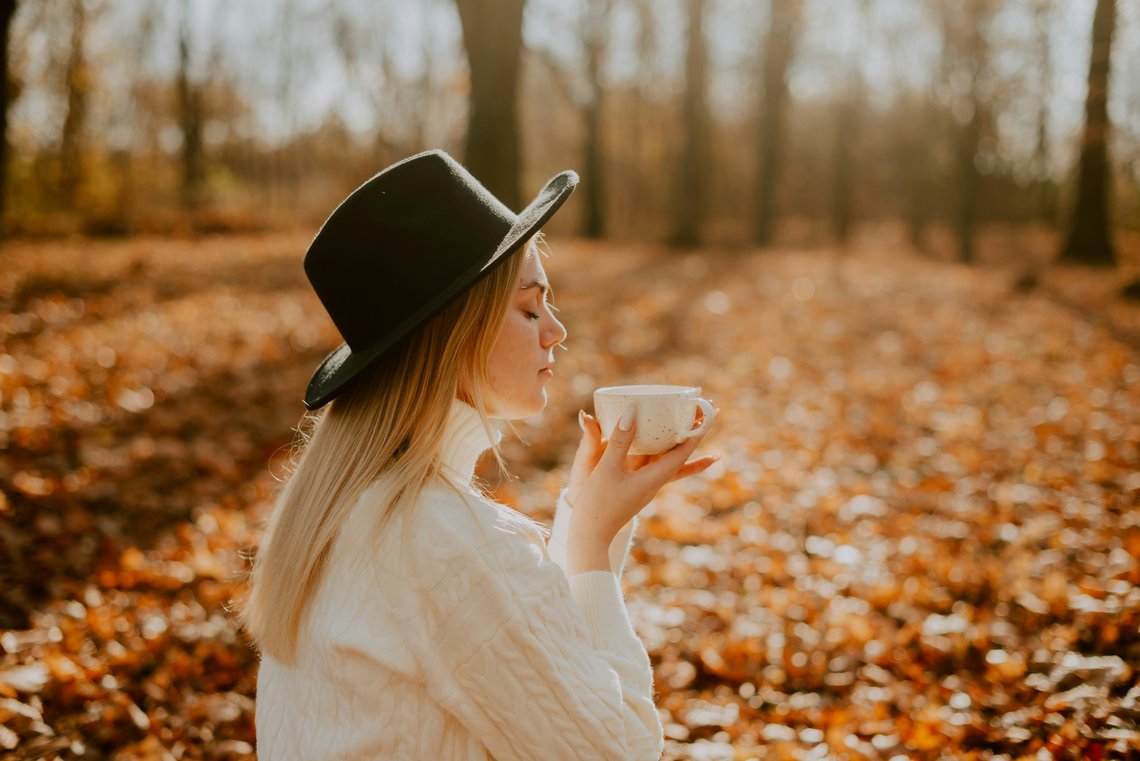 Frau im Herbstwald riecht an Teetasse Frau im Herbstwald riecht an Teetasse