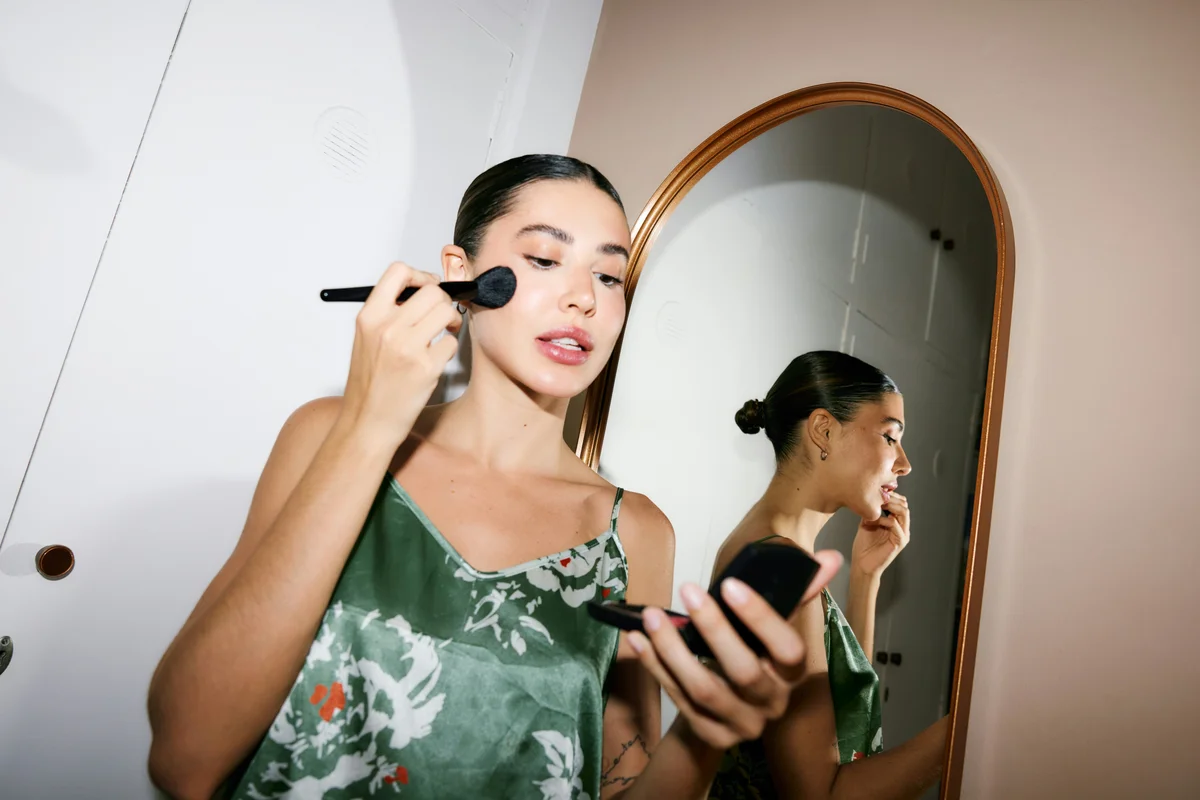 Frau trägt vor einem Spiegel mit einem Pinsel Make-up auf und macht sich ohne besonderen Anlass fertig.