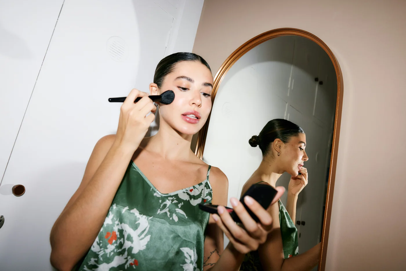 Frau trägt vor einem Spiegel mit einem Pinsel Make-up auf und macht sich ohne besonderen Anlass fertig.