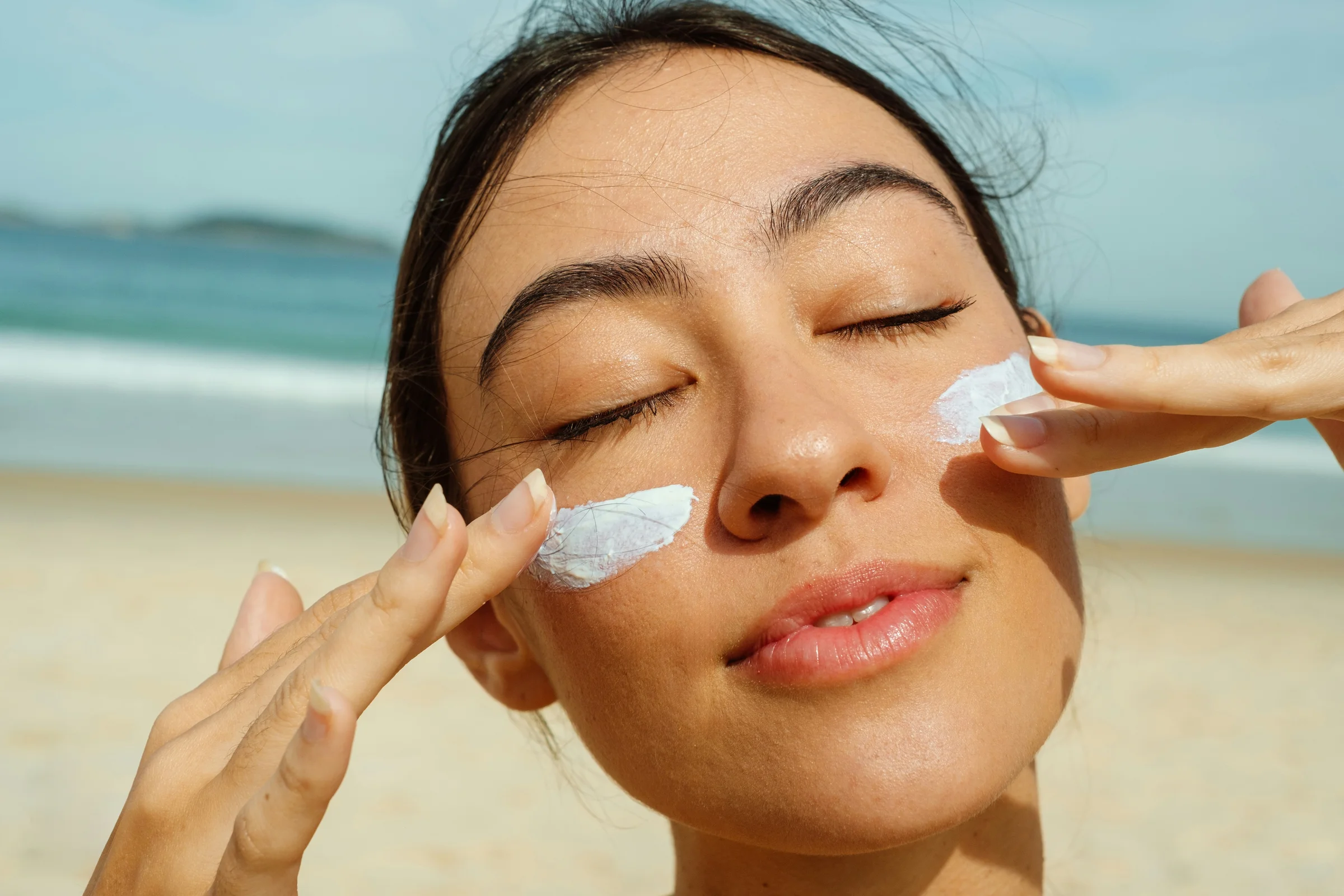 Porträt einer Frau am Strand mit Sonnencreme im Gesicht