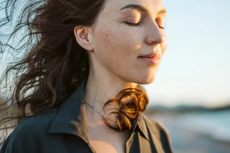 Frau mit natürlich wirkenden Sommersprossen im warmen Sonnenlicht als Inspiration für den Fake-Freckles-Look.