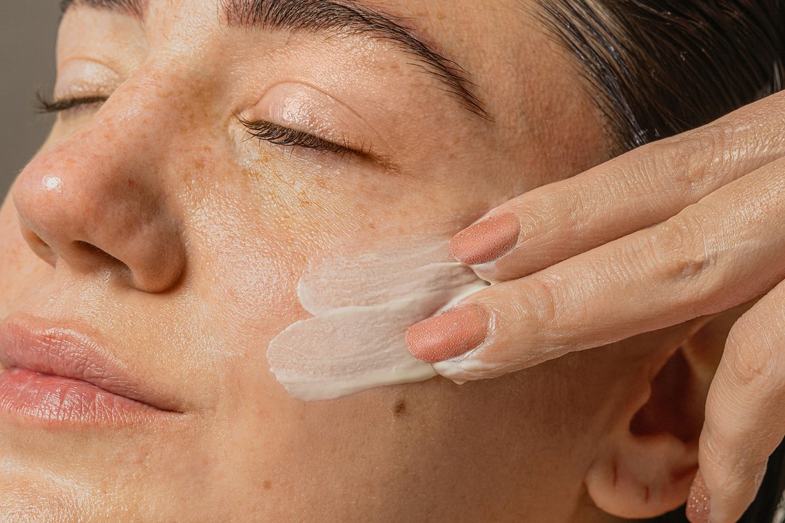 Frau trägt BB Cream mit den Fingern auf die Wange auf, Nahaufnahme der cremigen Textur auf der Haut.