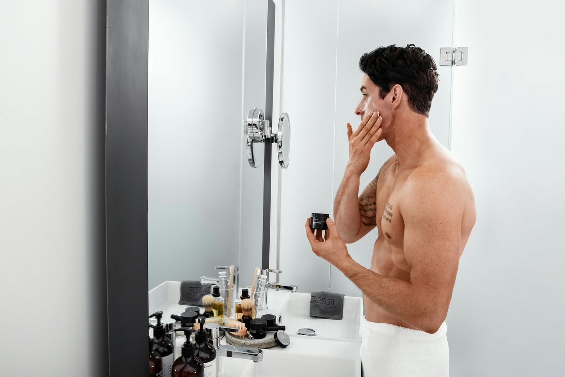 Mann im Bad cremt sich das Gesicht ein mit Anti Aging Creme für Männer Mann im Bad cremt sich das Gesicht ein mit Anti Aging Creme für Männer
