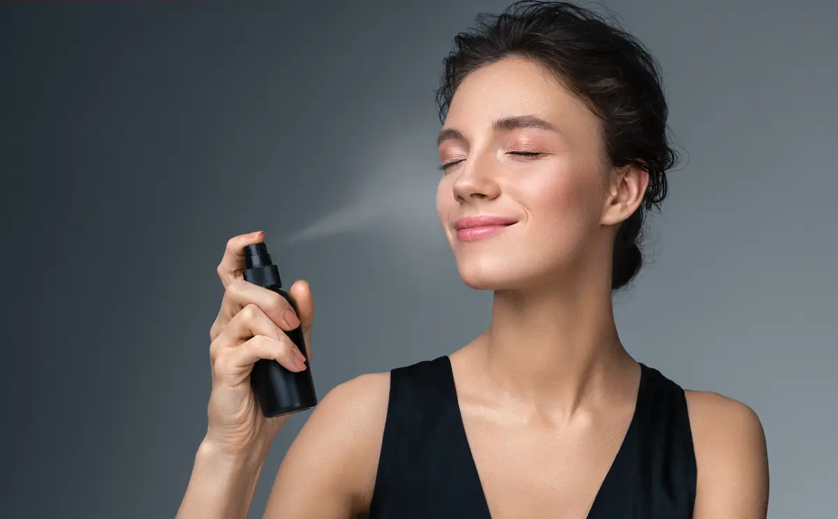 Frau sprüht Fixing Spray auf ihr Gesicht