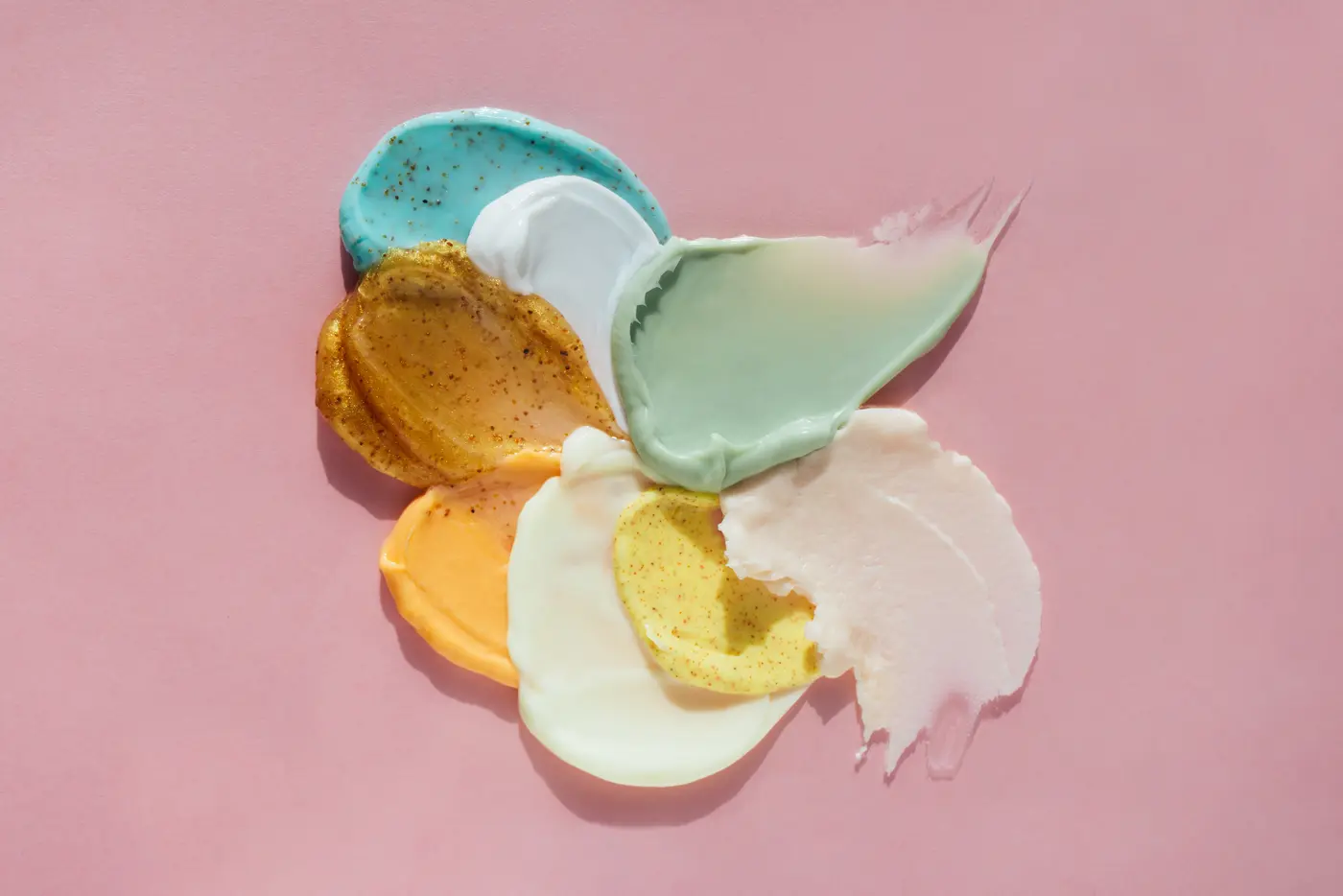 Kleckse von Kosmetikprodukten verschiedener Farben und Texturen auf rosa Hintergrund
