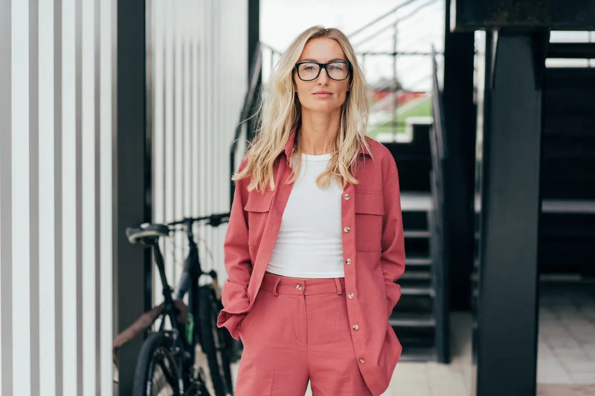 Porträt einer eleganten blonden, selbstbewussten Frau mit Brille, die steht und in die Kamera schaut