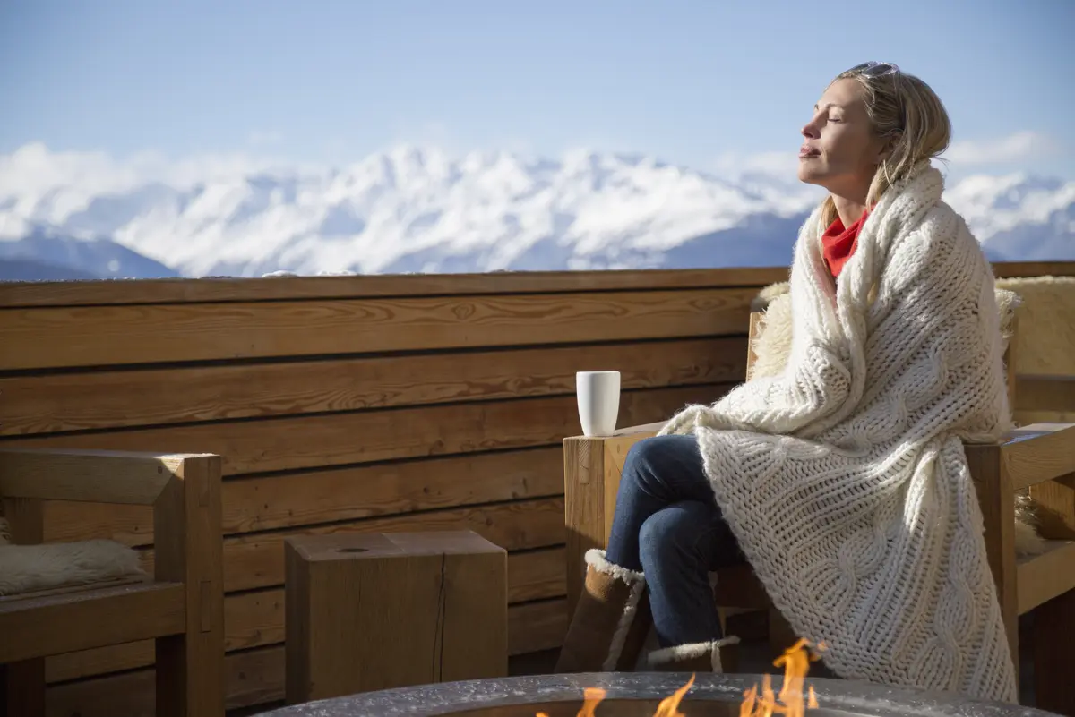 Junge Frau sitzt auf dem Balkon einer Ski-Lodge und genießt die Sonne