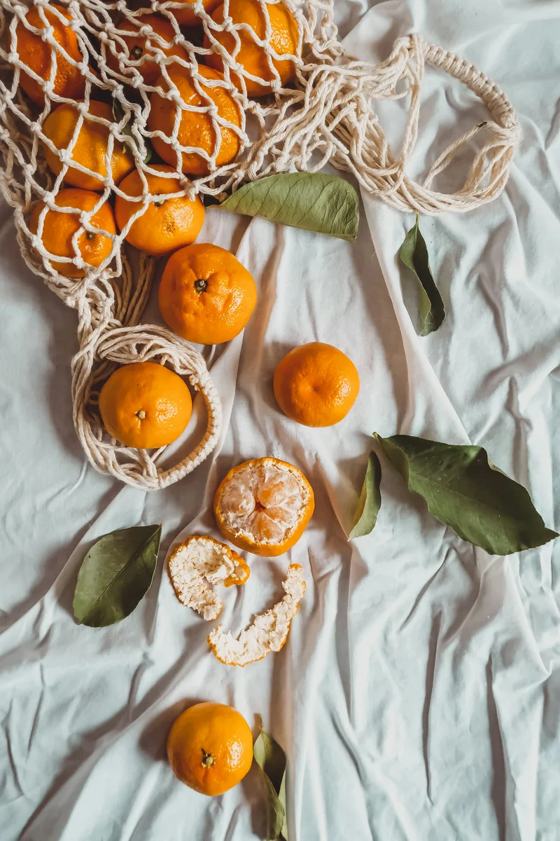 Frische Mandarinen im Netz auf weißem Stoff – sommerliche Inspiration für Mandarinen-Parfums