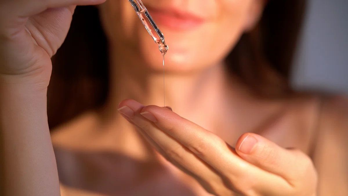 Frau tropft ein klares Hyaluron-Serum aus einer Glaspipette auf ihre Fingerspitzen
