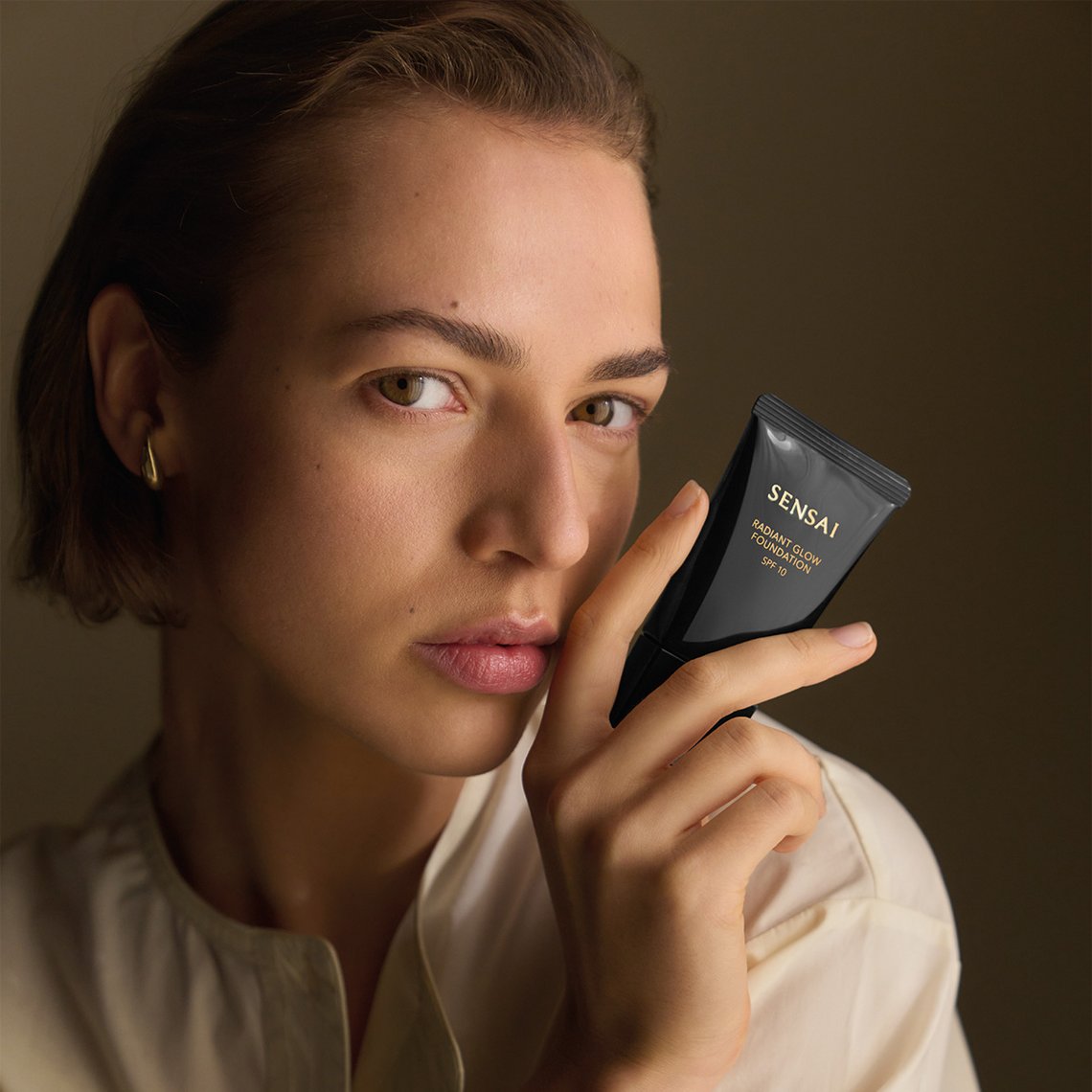 Frau mit Radiant Glow Foundation von Sensai in der Hand