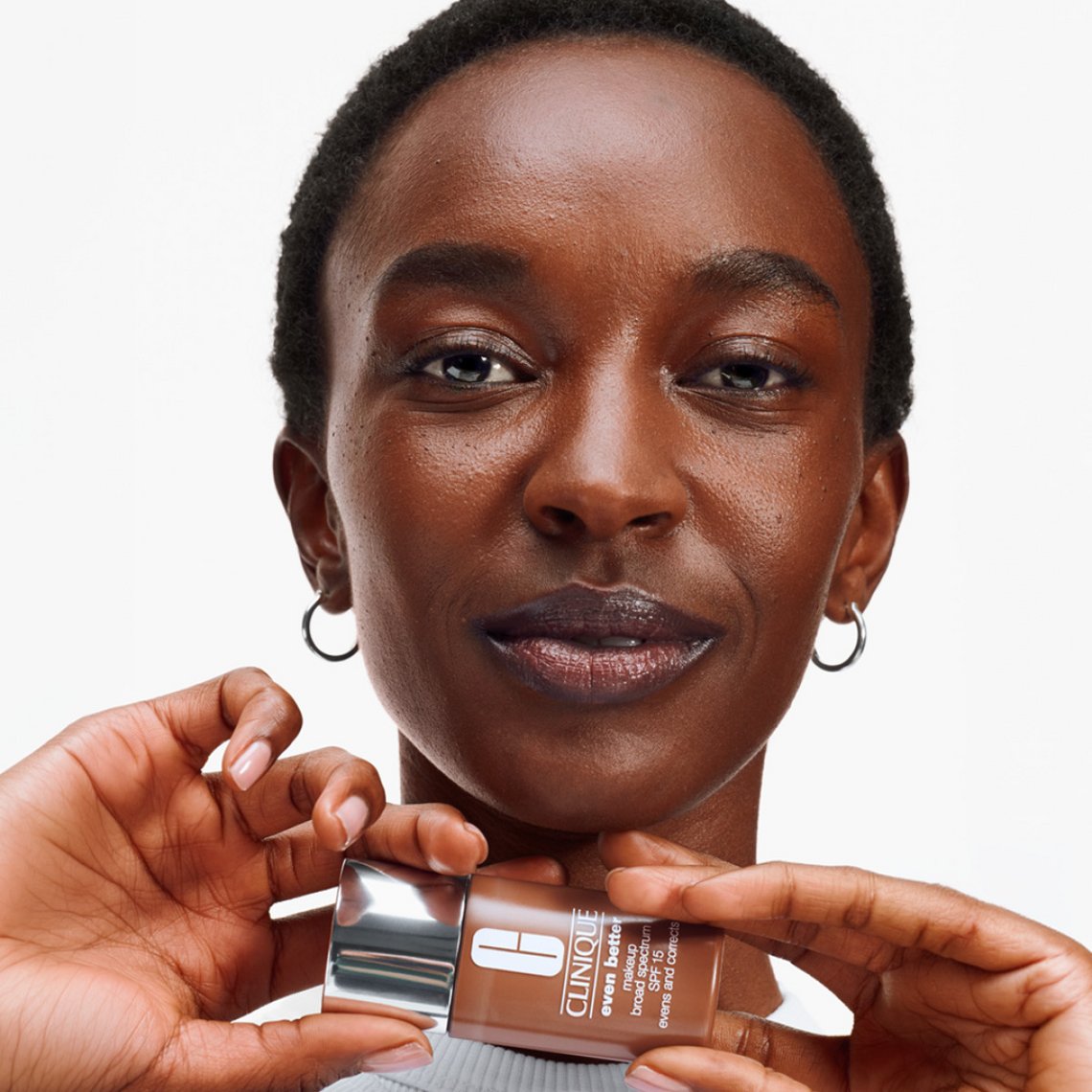 Frau mit dunkler Hautfarbe hält Clinique Even Better Makeup SPF 15 Flakon in passender Nuance