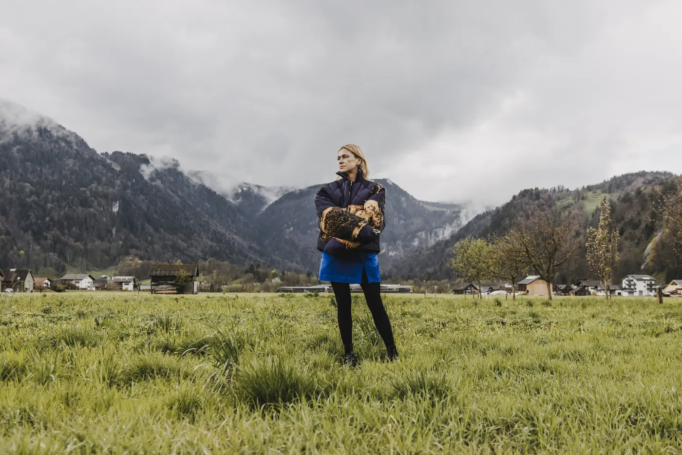 Eine Frau steht auf einer grünen Wiese, im Hintergrund ne Bergkulisse
