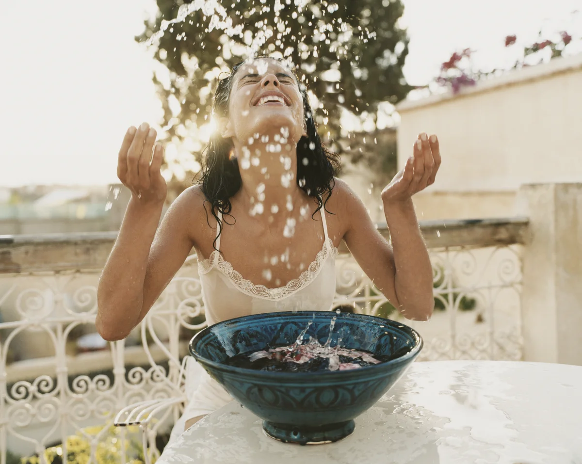 Frau spritzt sich Wasser ins Gesicht