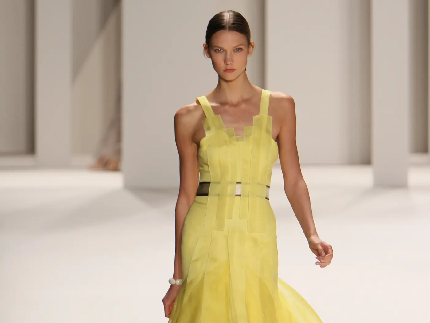 Ein Model in einem gelben Kleid läuft einen Laufsteg entlang