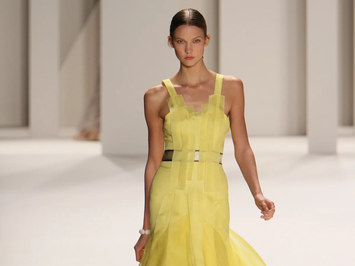 Ein Model in einem gelben Kleid läuft einen Laufsteg entlang