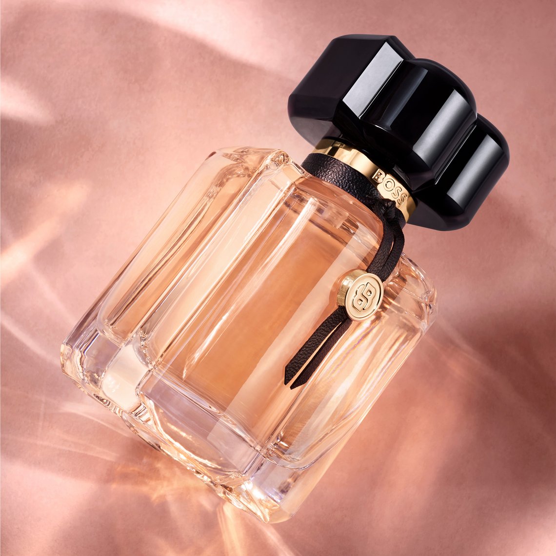 BOSS Bottled Beyond Eau de Parfum Flakon in Nahaufnahme, schräg liegend auf rosé-goldenem Hintergrund mit Lichtreflexen