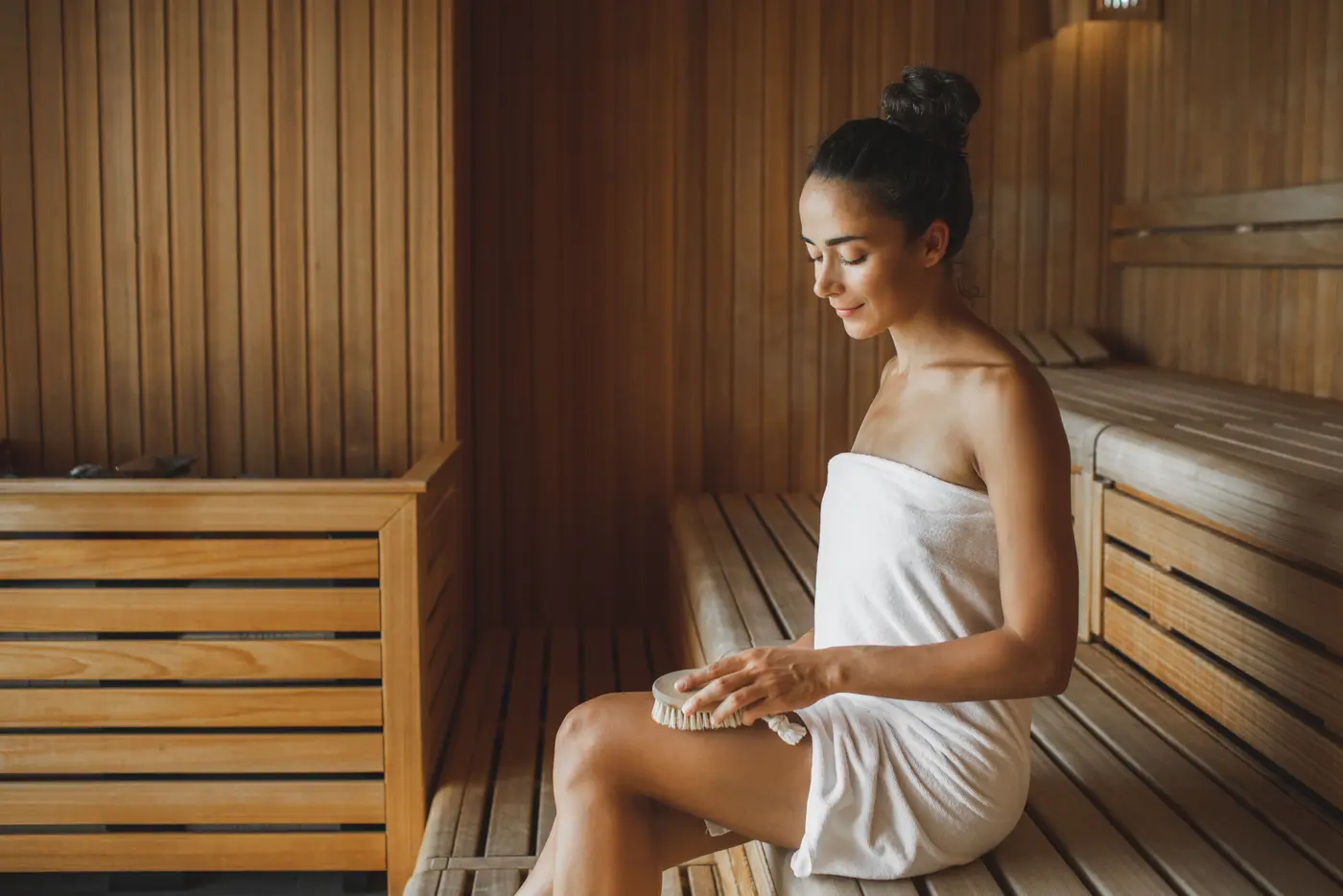 Junge Frau sitzt in der Sauna mit einer Körperbürste
