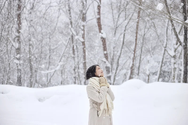 Eine Japanerin mit Schal steht in einem verschneiten Winterwald