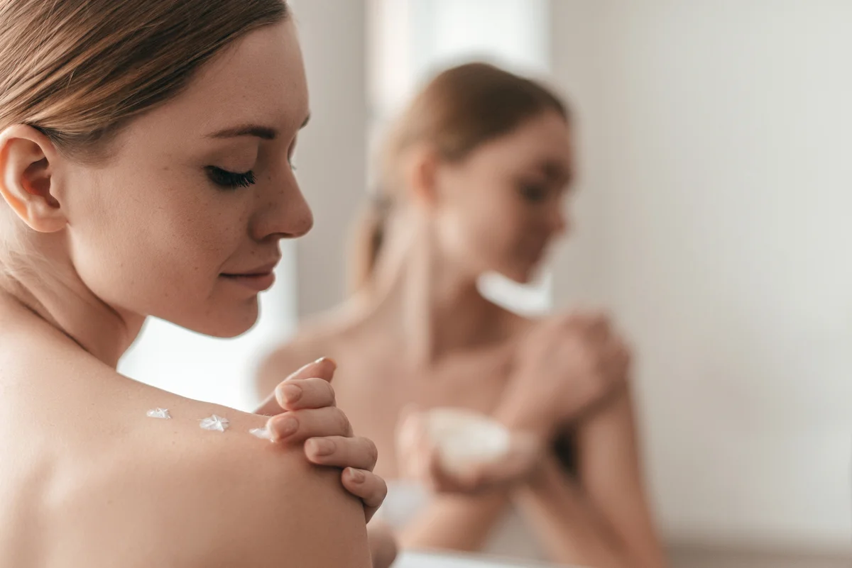 Junge Frau tupft sich Body Lotion auf die Schulter