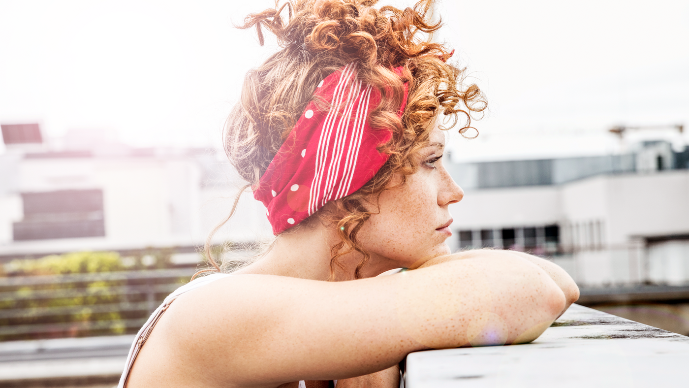 Rothaarige Frau mit Locken und rotem Bandana schaut in die Ferne