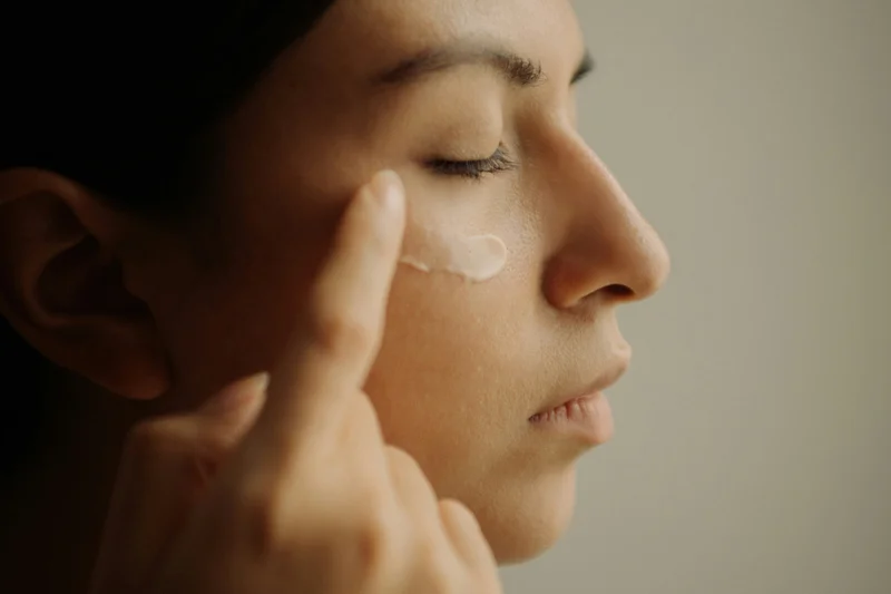 Frau mit geschlossenen Augen tupft Hyaluron-Augencreme unter das Auge auf
