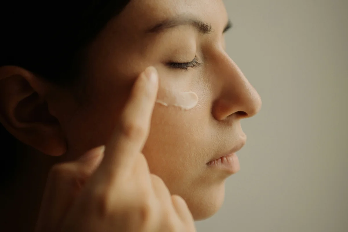 Frau mit geschlossenen Augen tupft Hyaluron-Augencreme unter das Auge auf