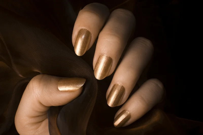 Hand mit goldenem Lack auf den Fingernägeln vor schwarzem Hintergrund