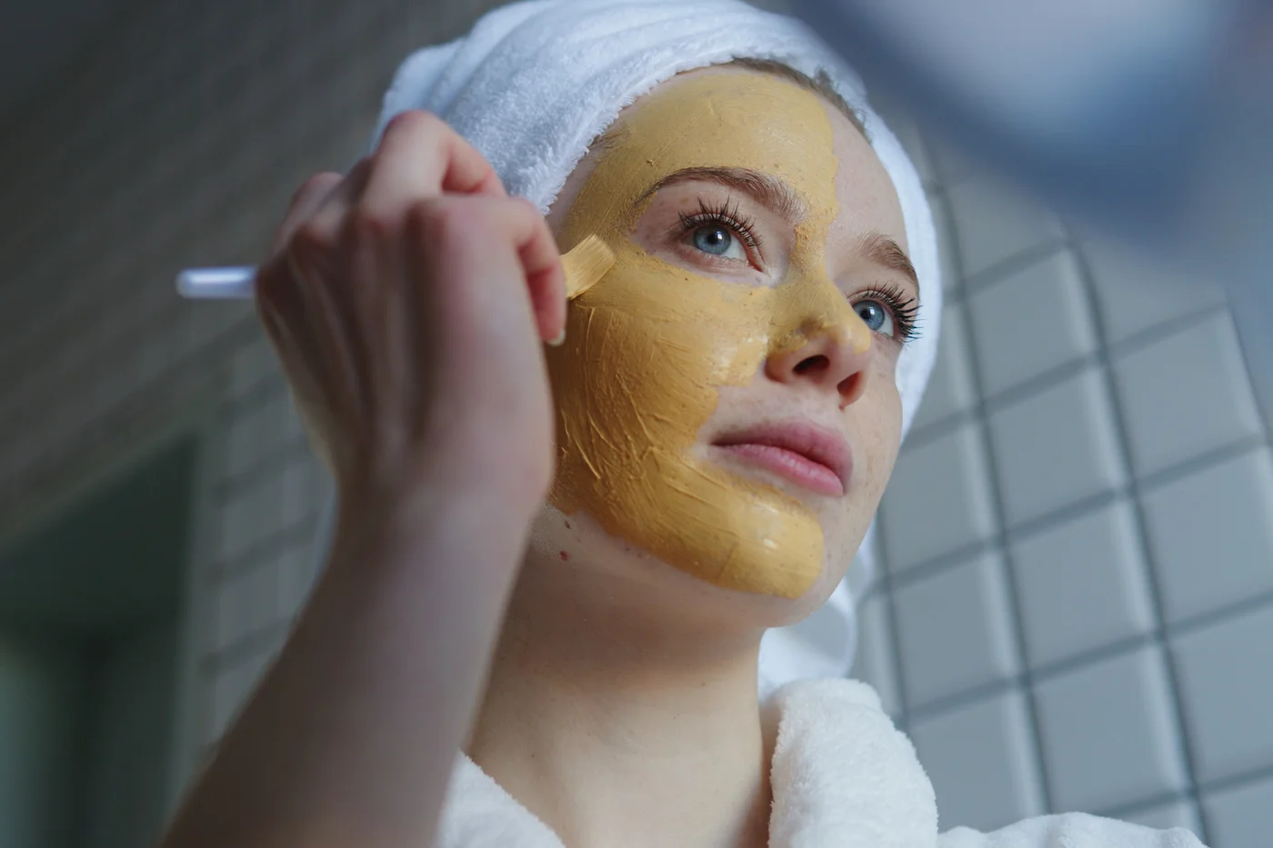 frau-im-bademantel-trägt-strukturierte-kurkuma-maske-auf