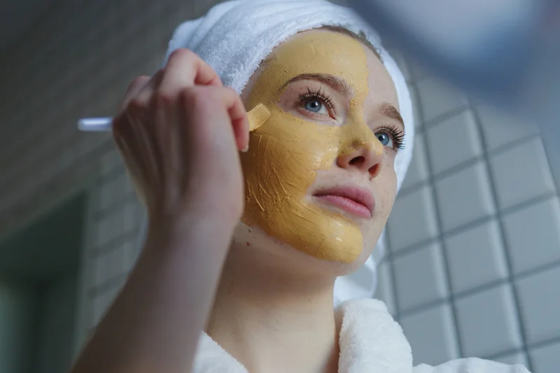 frau-im-bademantel-trägt-strukturierte-kurkuma-maske-auf