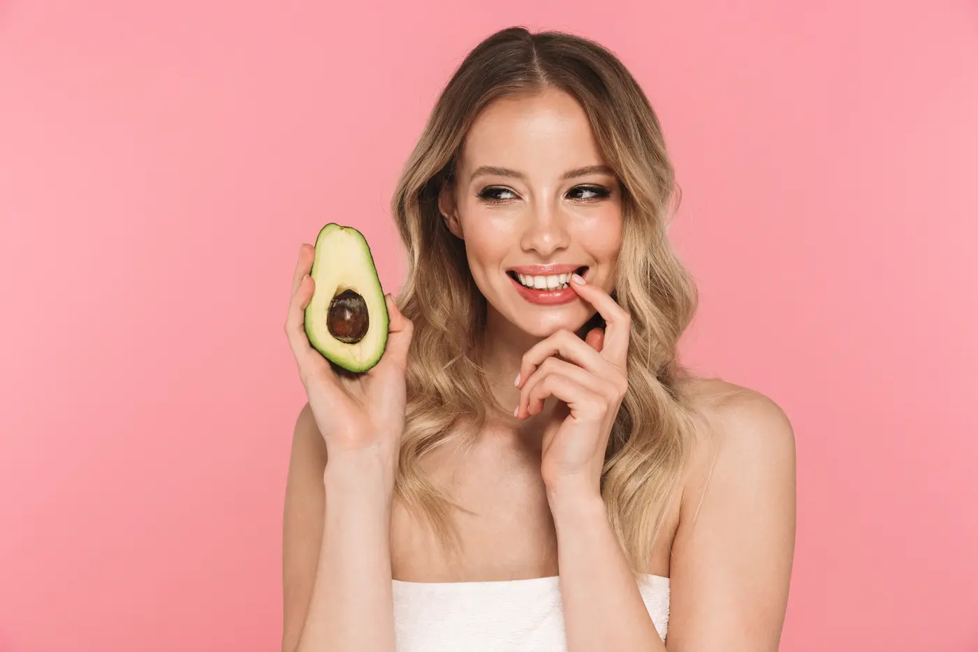 Junge Frau hält Avocado vor rosa Hintergrund