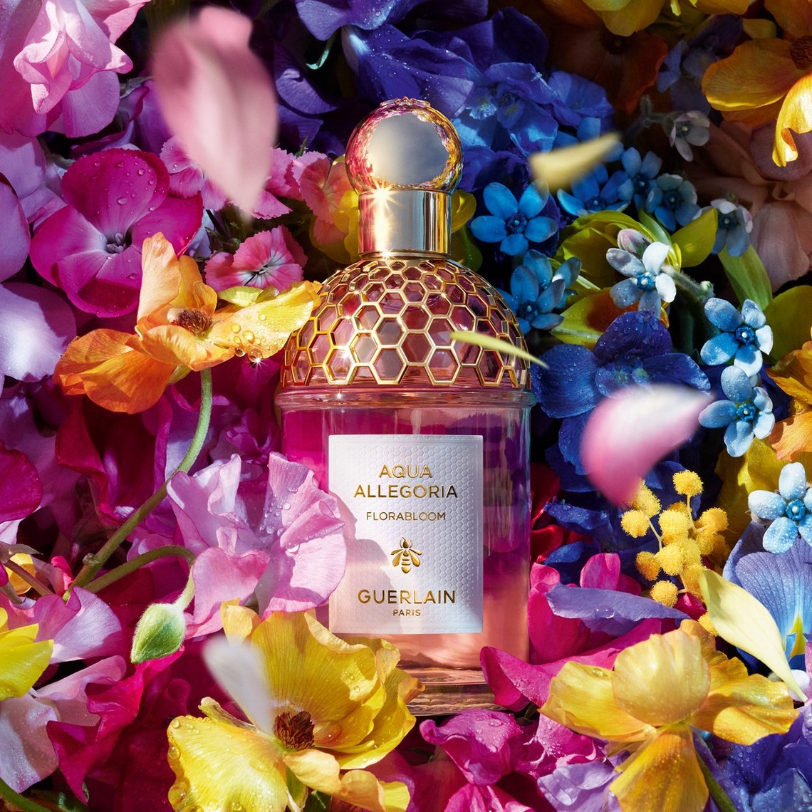 Guerlain Aqua Allegoria Florabloom Eau de Toilette Flakon mit weißem Etikett, eingebettet in ein lebendiges Arrangement aus bunten Frühlingsblumen.